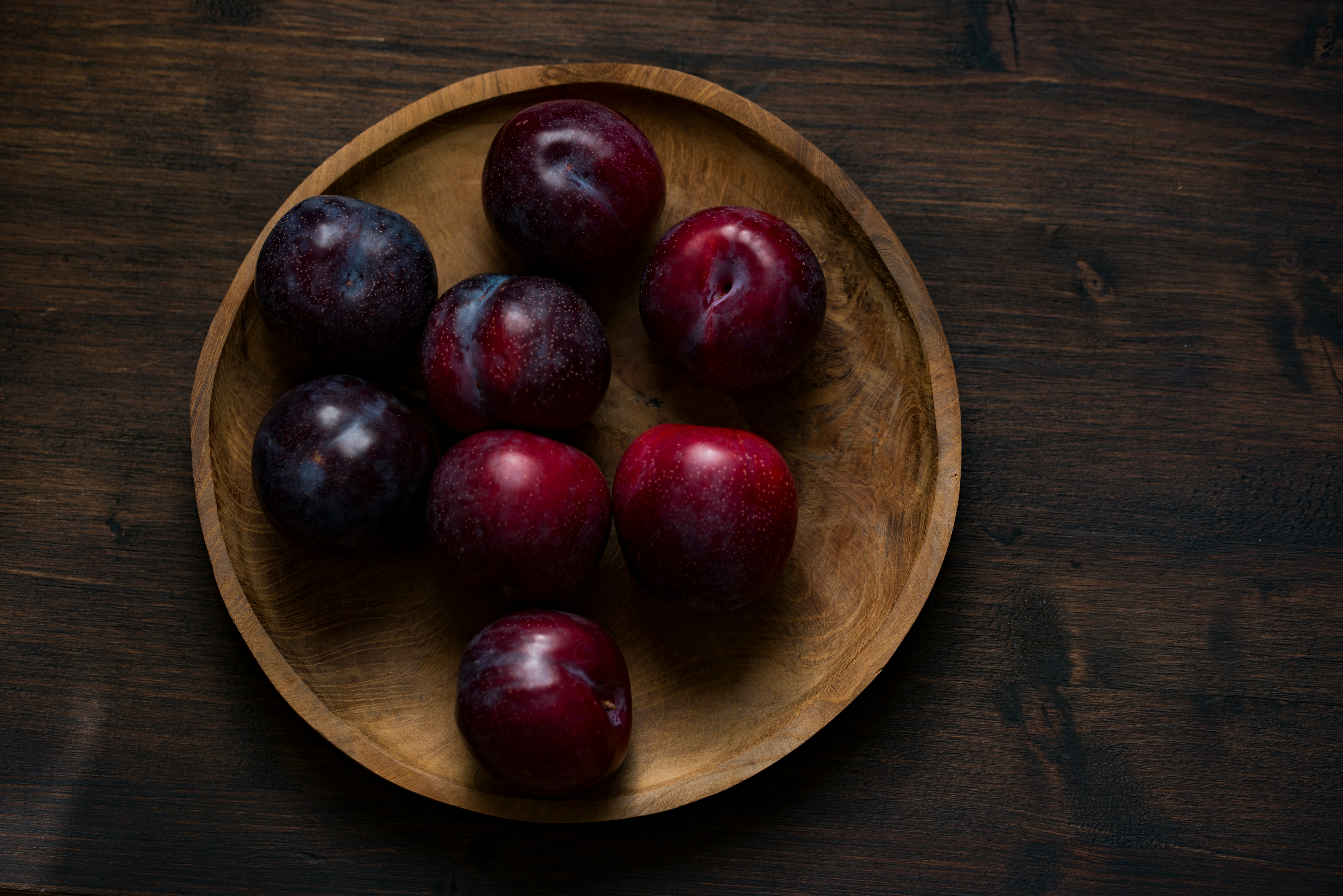 red plum fruits on round brown wooden plate