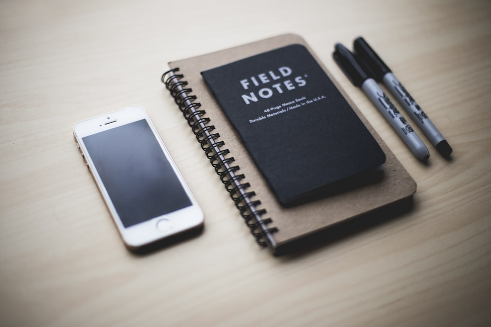 iPhone 5s plateado cerca del libro Field Notes