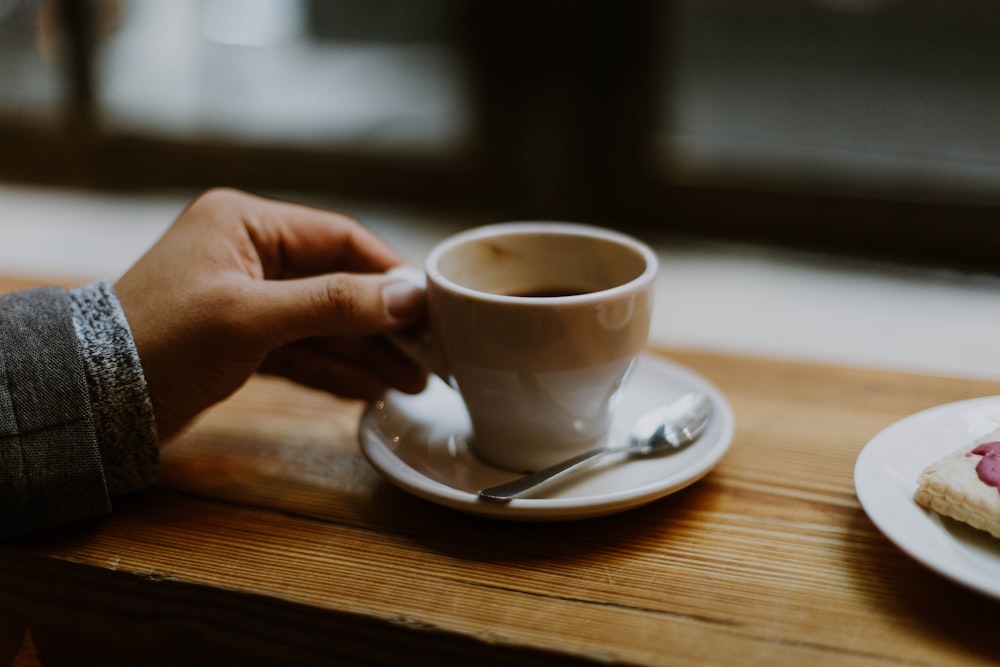 persona sosteniendo una taza de té de cerámica blanca