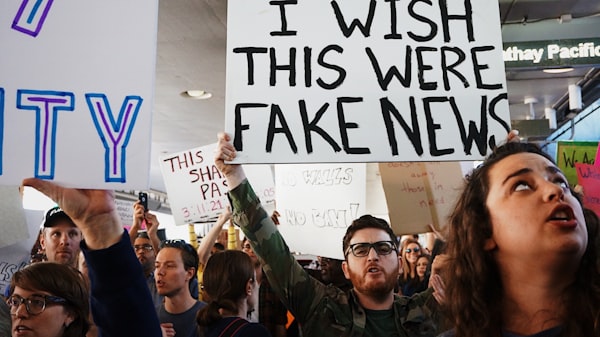 people at a protest, with the most prominent sign reading "I wish this were fake news"