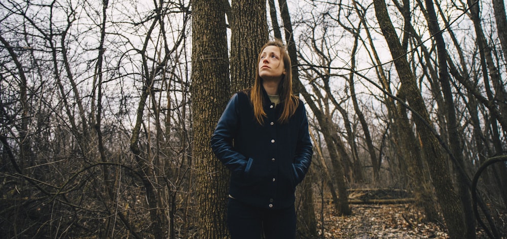 woman staring up while leaning on brown tree