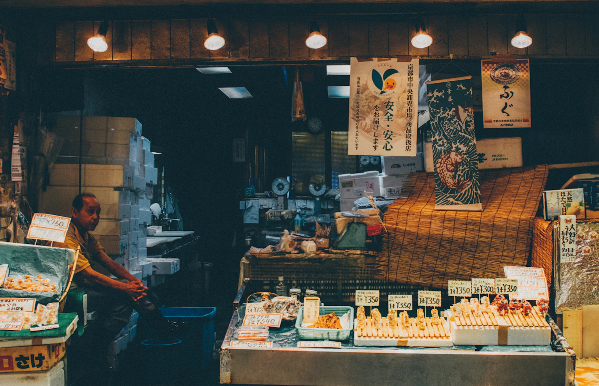 A shopkeeper sits among shelves of goods in a small, warmly lit store