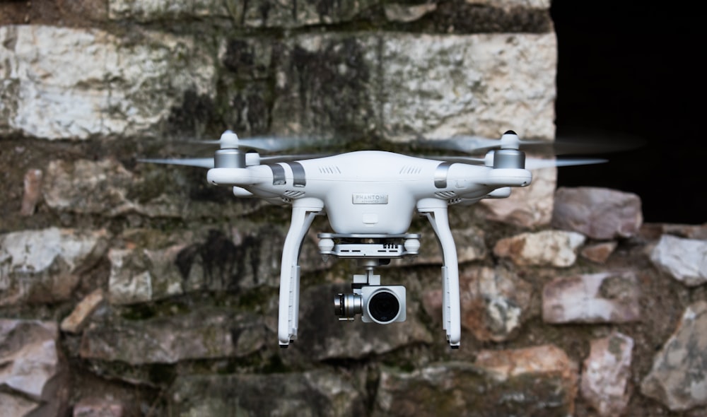 quadricoptère DJI blanc et argenté près d’un mur en béton brun pendant la journée