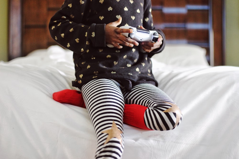 children holding gray game controller sitting on white bed