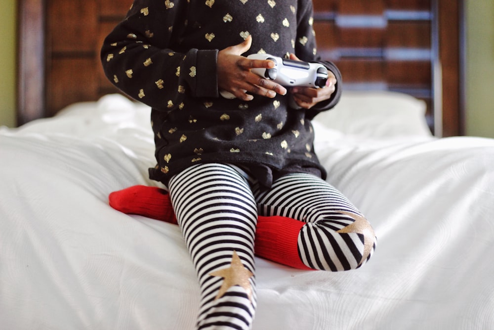 enfants tenant une manette de jeu grise assis sur un lit blanc