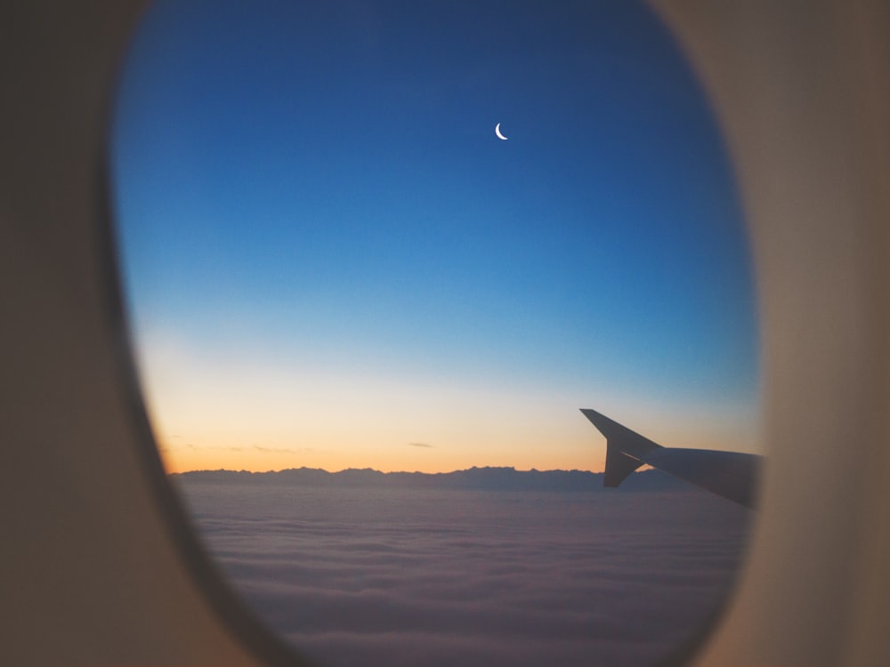 airplane window view of wing, clouds, and half moon
