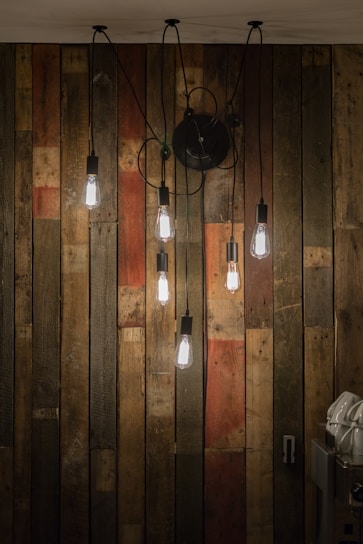 A warm, inviting display of vintage brass sconces and ship lights arranged on a rustic wooden wall.