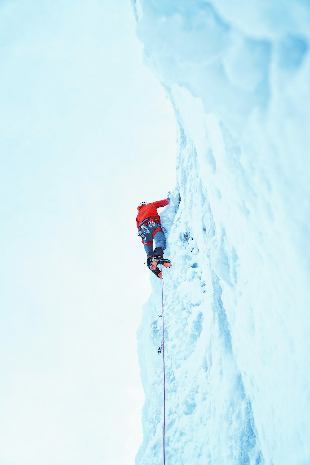 personne portant une veste rouge escalade sur un glacier