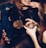 A group of people are gathered closely together, engaging in conversation and sharing drinks. One person with long hair is smiling and the focus is on hands holding glasses filled with beverages and ice. The setting appears to be a lively social environment, likely a bar or club.