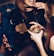 A group of people are gathered closely together, engaging in conversation and sharing drinks. One person with long hair is smiling and the focus is on hands holding glasses filled with beverages and ice. The setting appears to be a lively social environment, likely a bar or club.