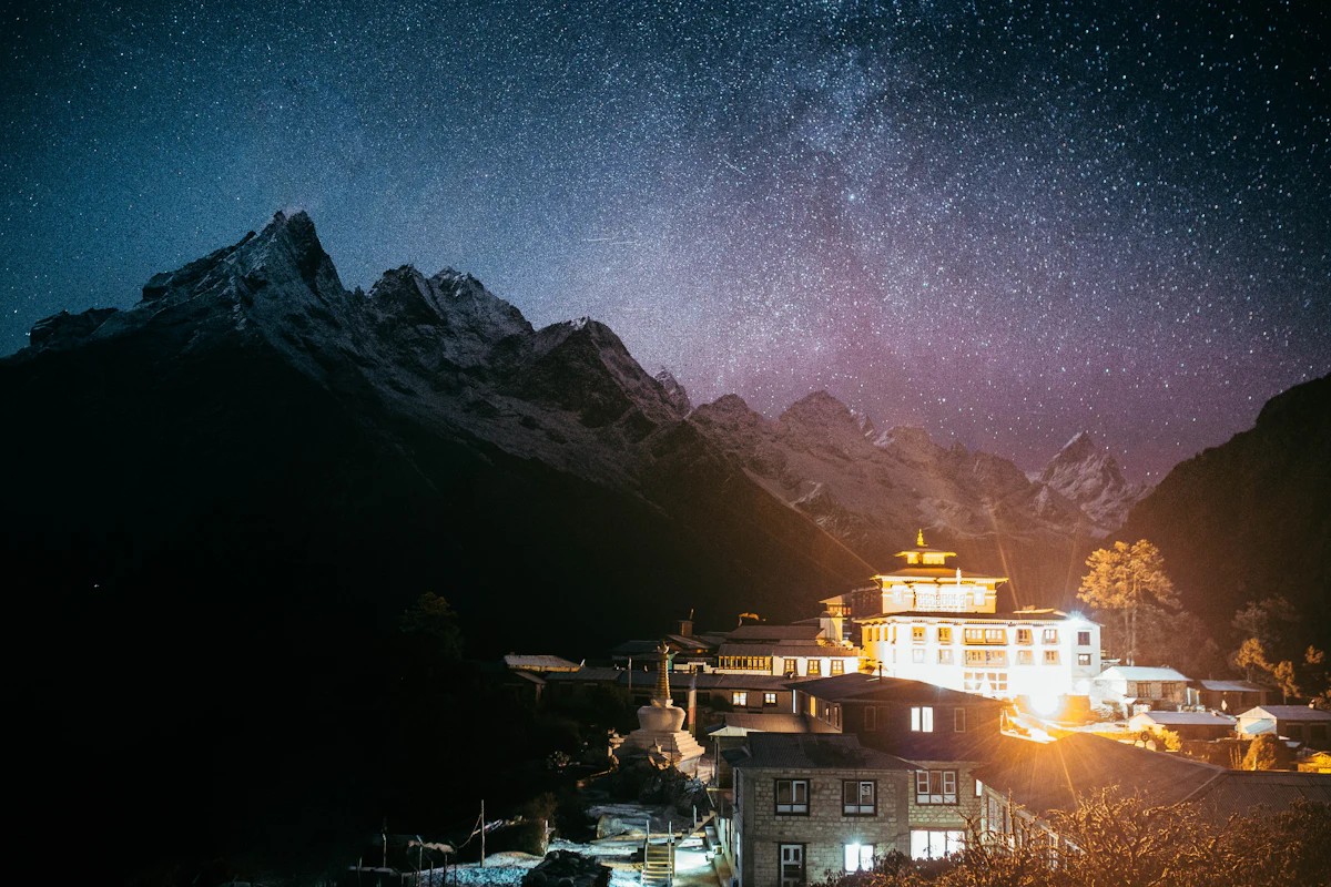 Tengboche Monastery lit up at night under the Milky Way, with dark peaks behind