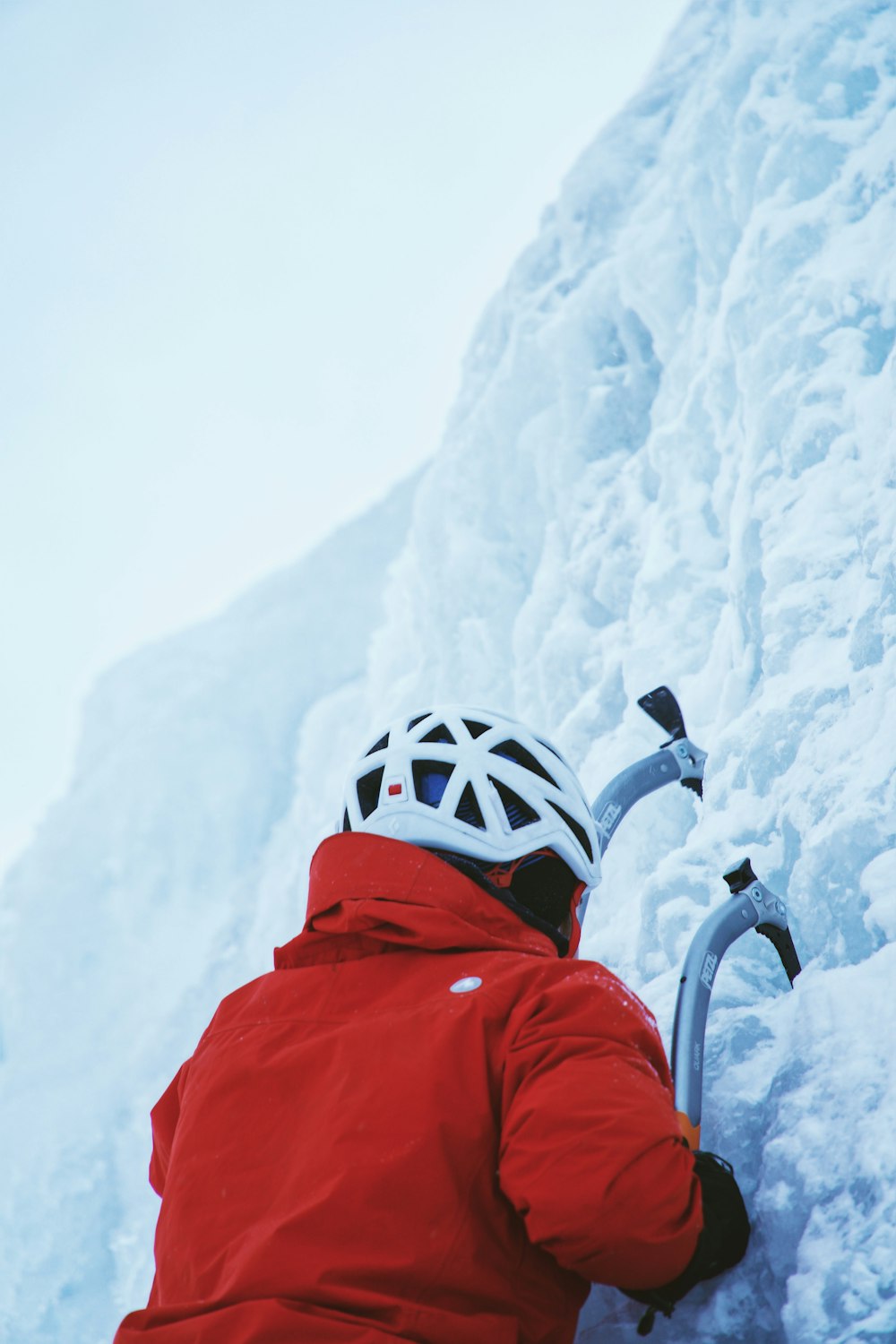 person in red jacket while climbing ice wall at daytime