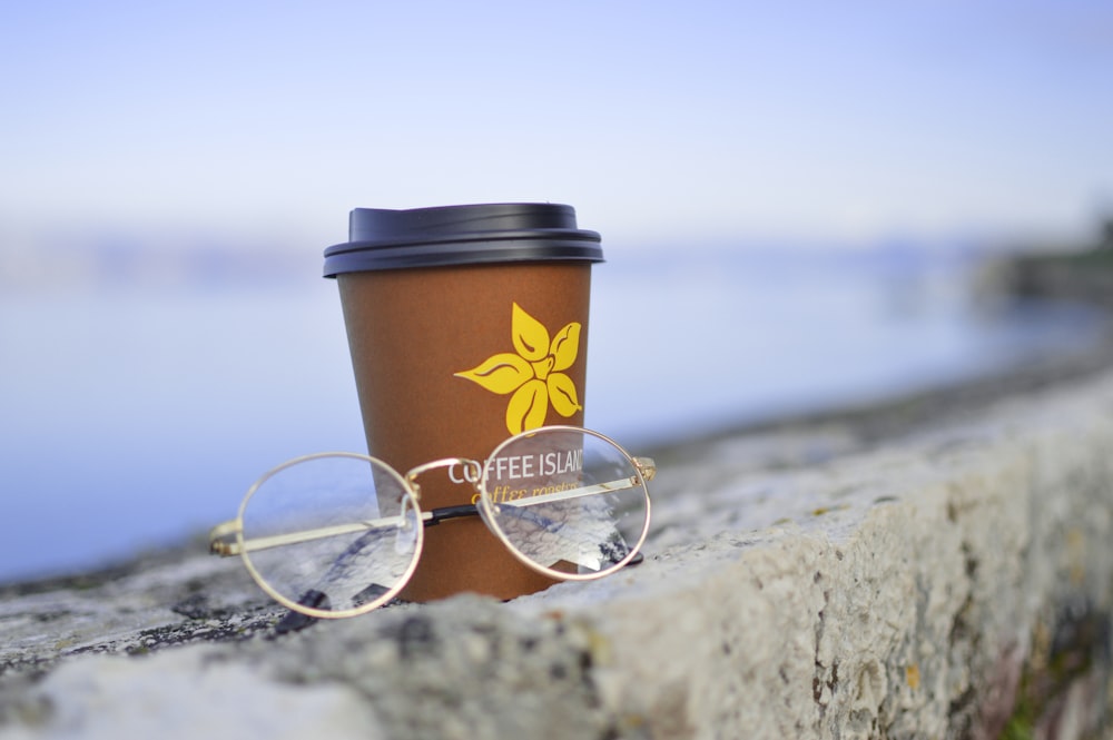 occhiali da vista con montatura color oro accanto a tazza usa e getta in plastica