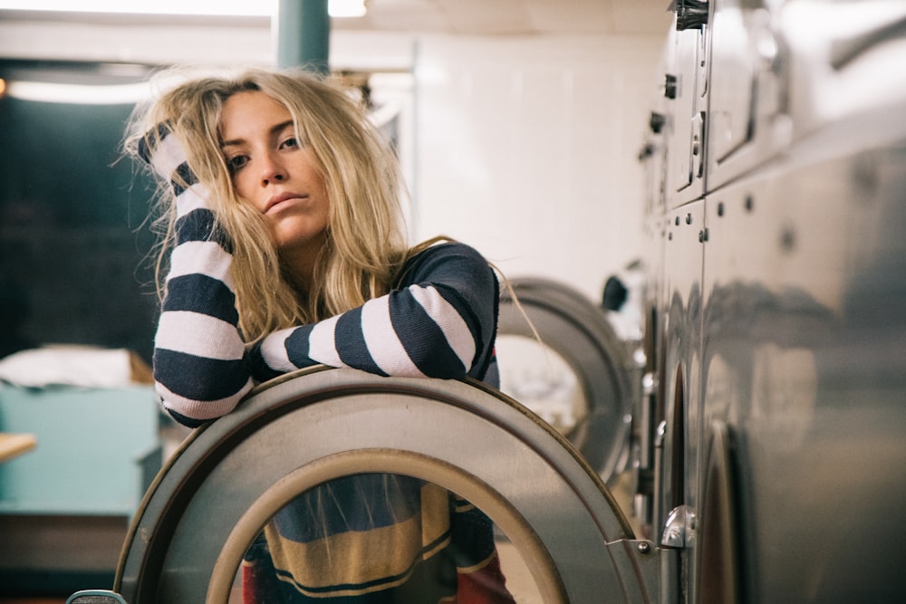 A blonde woman leaning against an open washing machine door in a laundromat