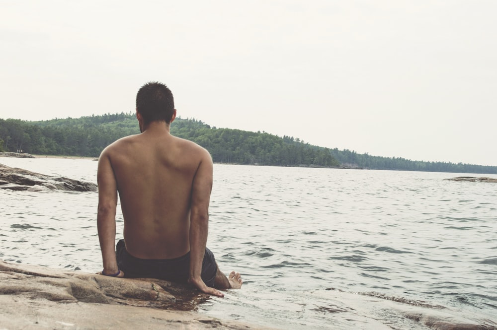 man wearing black shorts sitting on shoreline