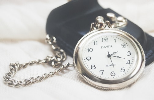 Close-up of a vintage silver pocket watch resting on a velvet cushion.