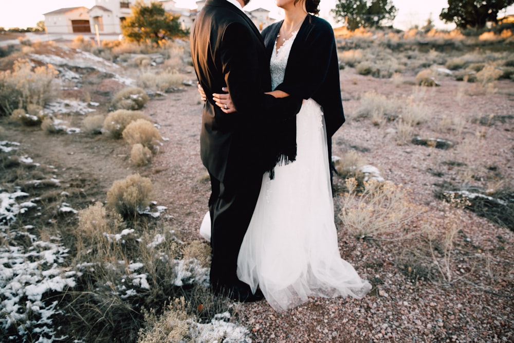 pareja de bodas de pie junto a la flor de pétalos blancos cerca de la casa blanca y los árboles durante el día