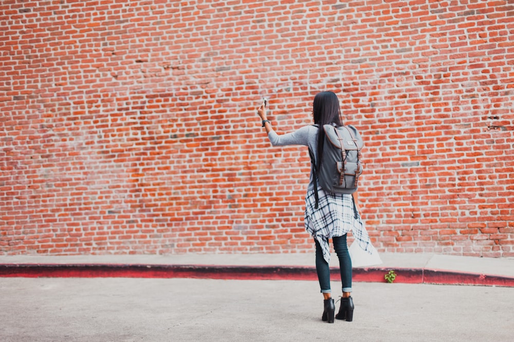 mulher em pé ao lado da parede de tijolo de cinza enquanto usa o smartphone