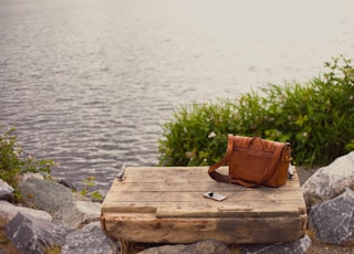 brown leather crossbody bag on brown wooden panel near water