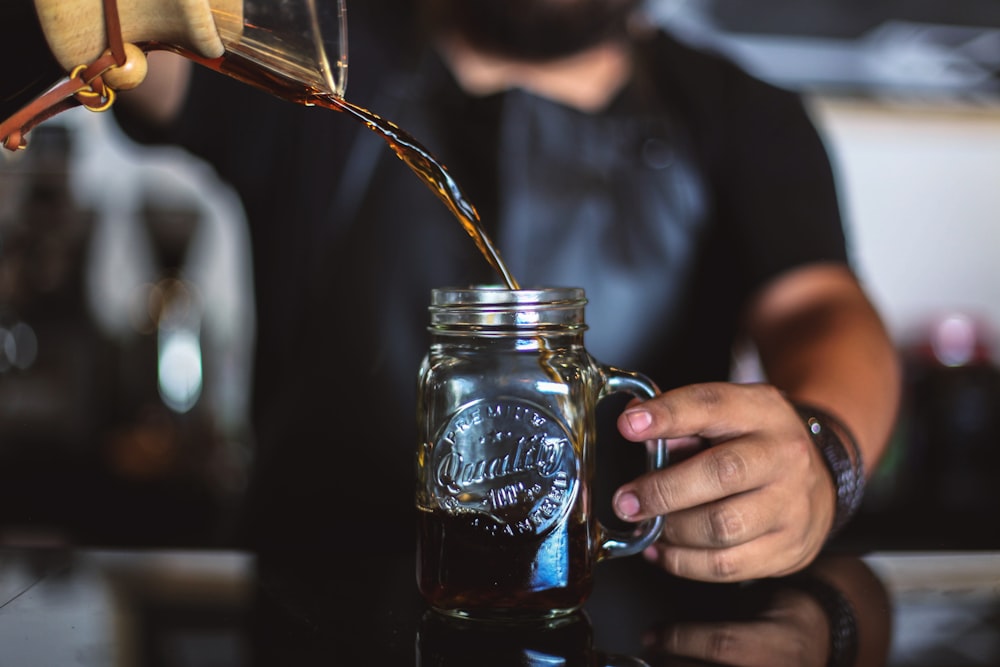 man pouring liquid on clear glass mason jar