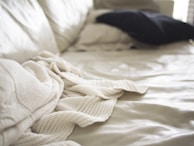 Close-up of a soft throw blanket casually draped over the edge of an upholstered platform bed.