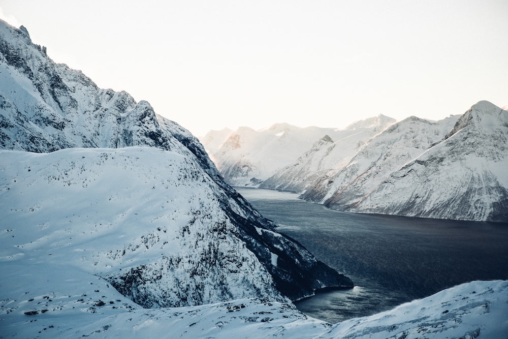 Fotografia de paisagem de montanhas cobertas de neve perto do corpo de água durante o dia