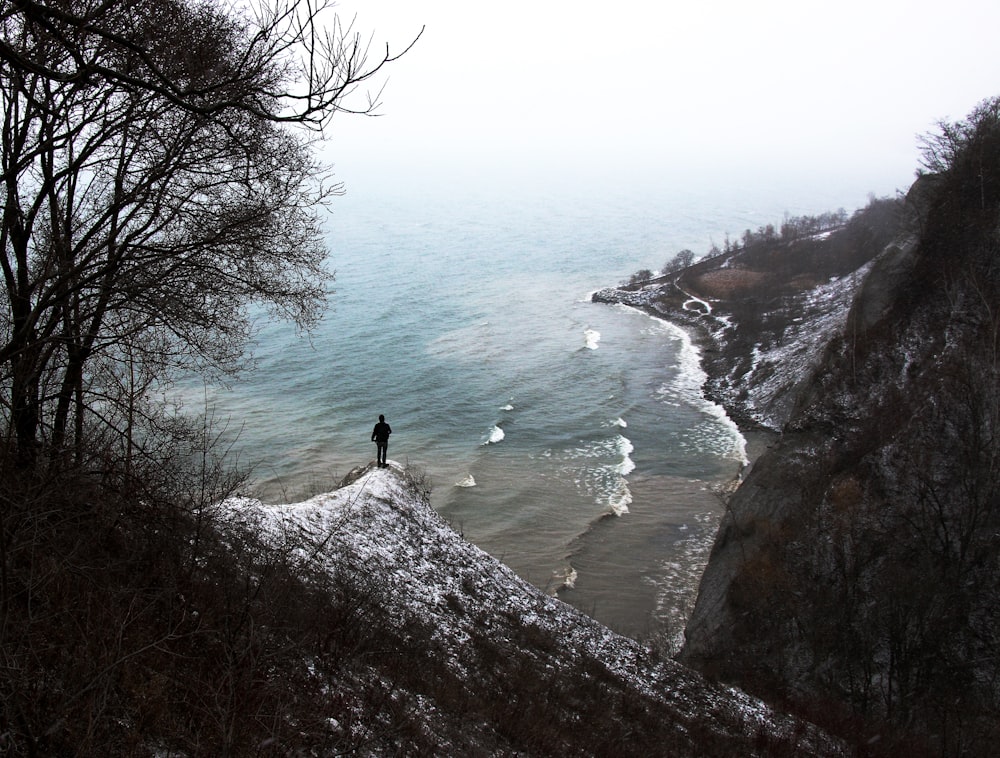 person standing on rock formation near the body of water