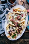 bacon strips and melted cheese topped fries on oval white and blue platter with gray stainless steel forks