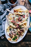 bacon strips and melted cheese topped fries on oval white and blue platter with gray stainless steel forks