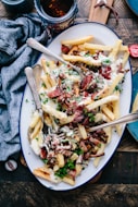 bacon strips and melted cheese topped fries on oval white and blue platter with gray stainless steel forks