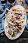 bacon strips and melted cheese topped fries on oval white and blue platter with gray stainless steel forks