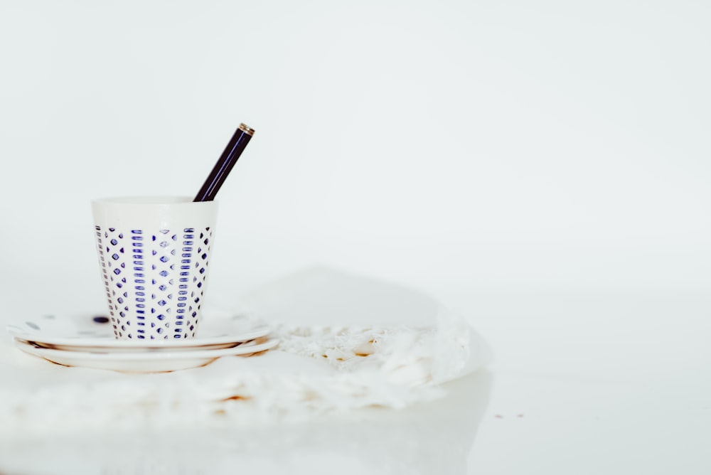 tazza bianca con penna su pannello bianco