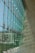 Large glass windows supported by metal brackets form a modern architectural facade, allowing an outside view of a park and buildings. The interior wall curves gracefully, casting intricate shadows on the floor.