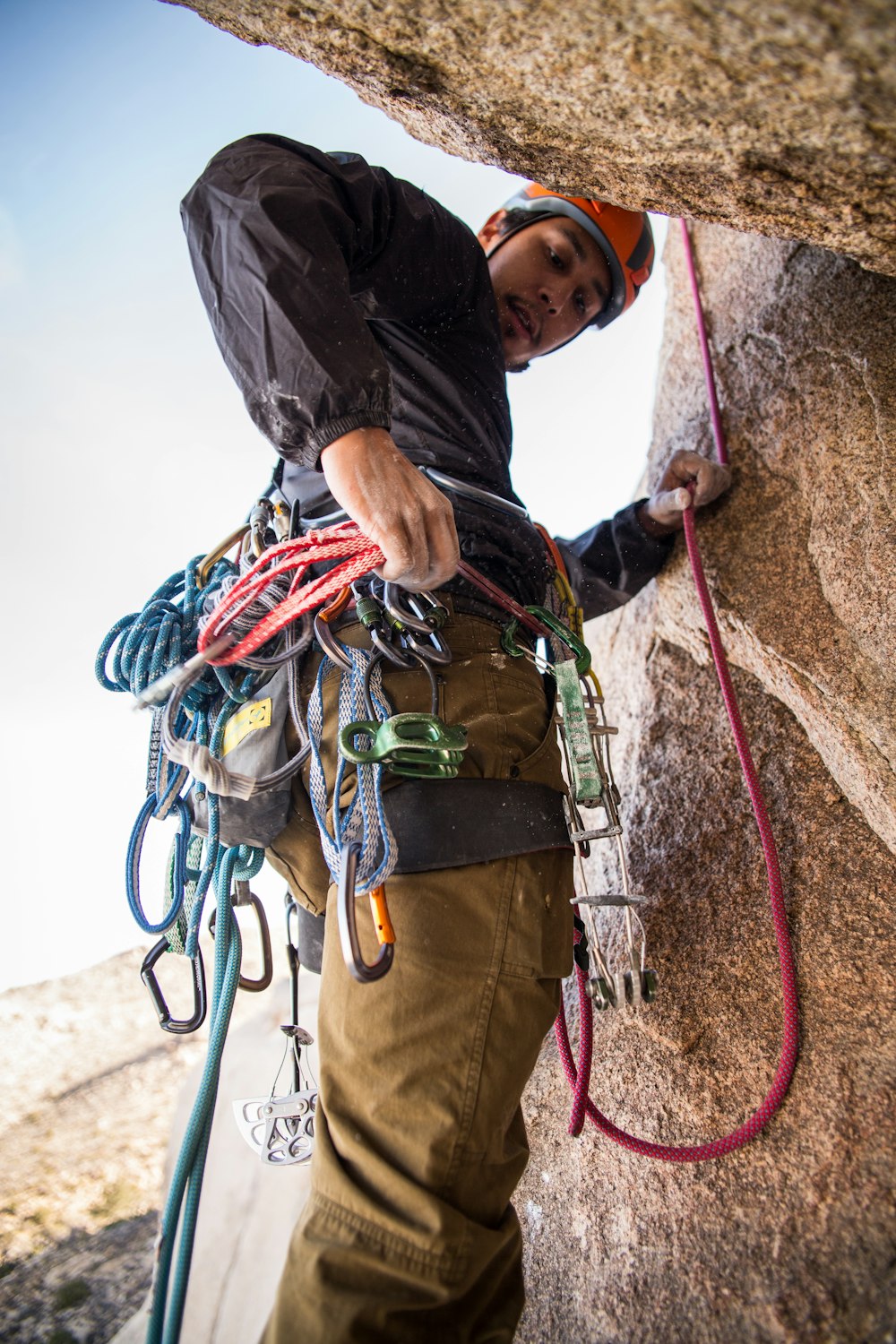 rock climber holding red rope strapped on waist while on side of brown boulder at daytime