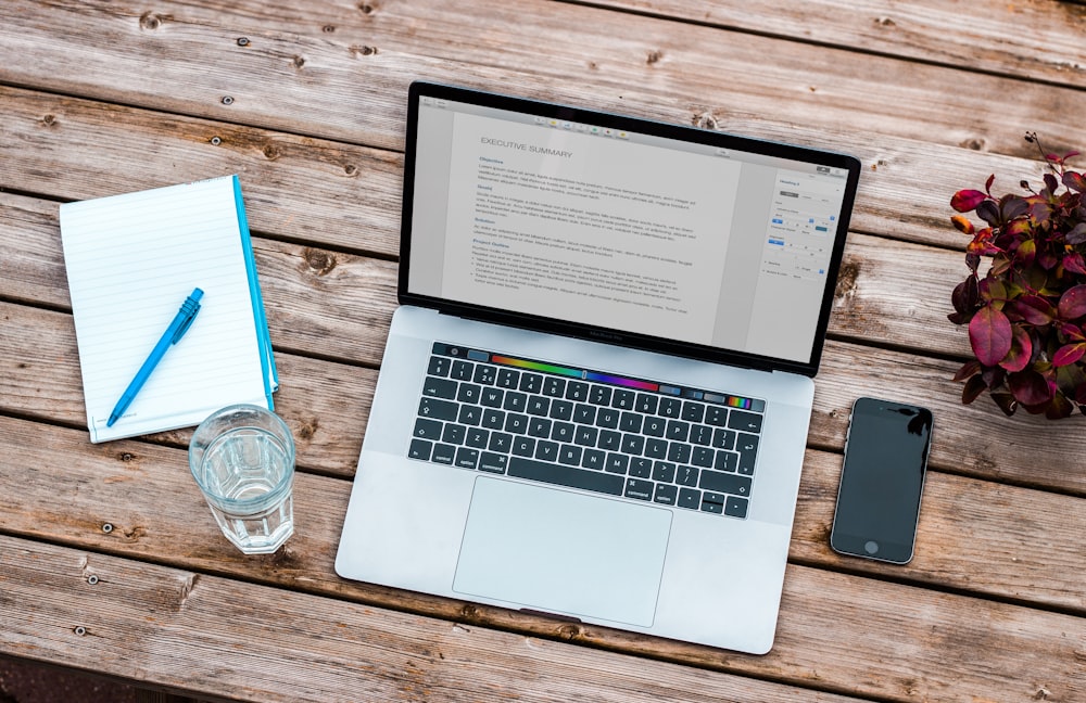 An overhead shot of a MacBook with a draft of an executive summary on a wooden surface