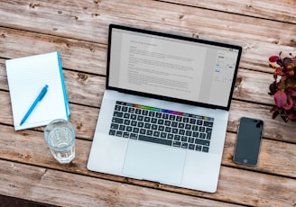 silver MacBook beside space gray iPhone 6 and clear drinking glass on brown wooden top