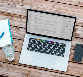 silver MacBook beside space gray iPhone 6 and clear drinking glass on brown wooden top