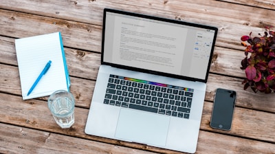 silver MacBook beside space gray iPhone 6 and clear drinking glass on brown wooden top