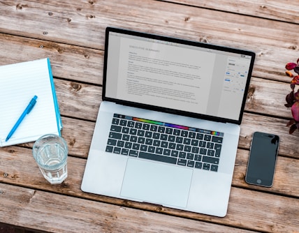 silver MacBook beside space gray iPhone 6 and clear drinking glass on brown wooden top