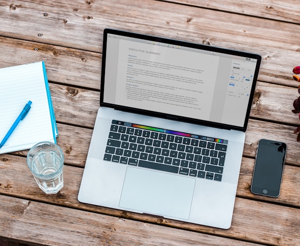 silver MacBook beside space gray iPhone 6 and clear drinking glass on brown wooden top