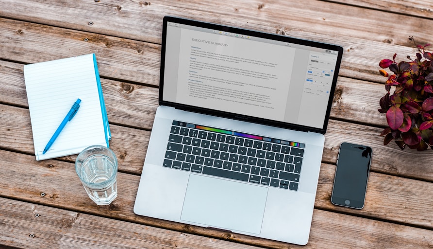 silver MacBook beside space gray iPhone 6 and clear drinking glass on brown wooden top