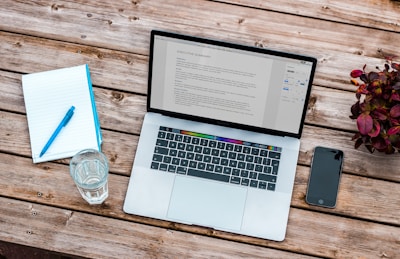 silver MacBook beside space gray iPhone 6 and clear drinking glass on brown wooden top