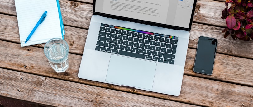 silver MacBook beside space gray iPhone 6 and clear drinking glass on brown wooden top