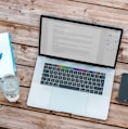 silver MacBook beside space gray iPhone 6 and clear drinking glass on brown wooden top