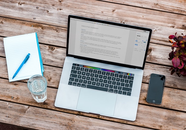 silver MacBook beside space gray iPhone 6 and clear drinking glass on brown wooden top