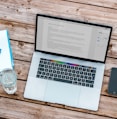 silver MacBook beside space gray iPhone 6 and clear drinking glass on brown wooden top