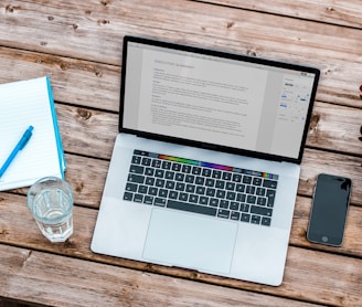 silver MacBook beside space gray iPhone 6 and clear drinking glass on brown wooden top