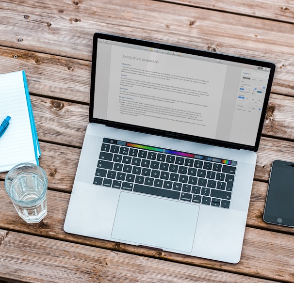 silver MacBook beside space gray iPhone 6 and clear drinking glass on brown wooden top