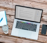 silver MacBook beside space gray iPhone 6 and clear drinking glass on brown wooden top