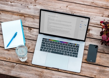 silver MacBook beside space gray iPhone 6 and clear drinking glass on brown wooden top